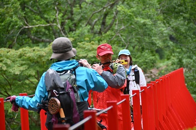 登山者が新緑に映える赤い橋を笑顔で渡っていました