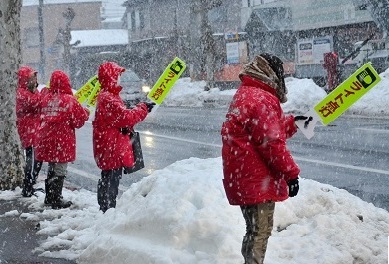 雪が降る中看板を掲げ、運転手に安全運転を呼び掛けていました