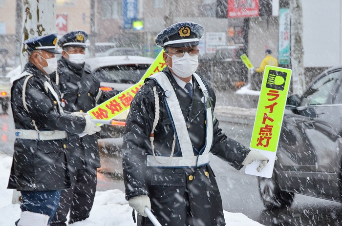 雪が降る中、手持ち看板を掲げ安全運転を呼び掛けていました